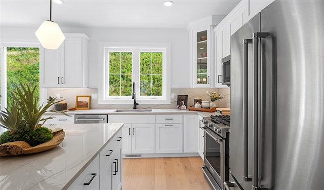 kitchen with white cabinets, high quality appliances, backsplash, light stone countertops, and a sink