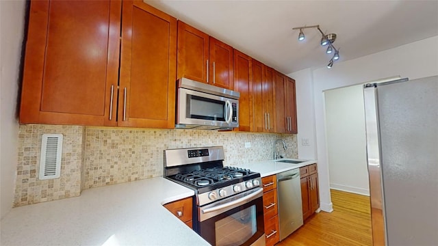 kitchen with stainless steel appliances, sink, decorative backsplash, and light hardwood / wood-style flooring