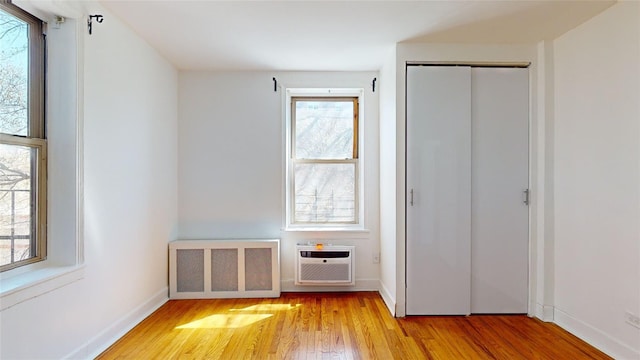 unfurnished bedroom featuring radiator, light hardwood / wood-style floors, a closet, and a wall mounted AC