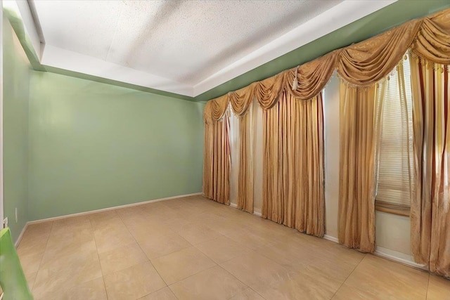 tiled spare room featuring a raised ceiling and a textured ceiling