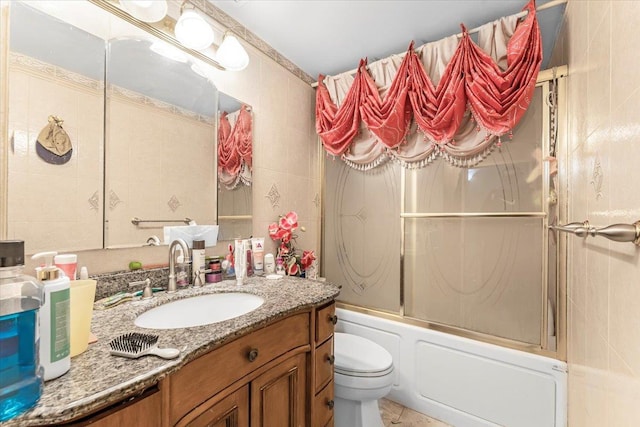 full bathroom featuring toilet, vanity, shower / bath combination with glass door, and tile walls