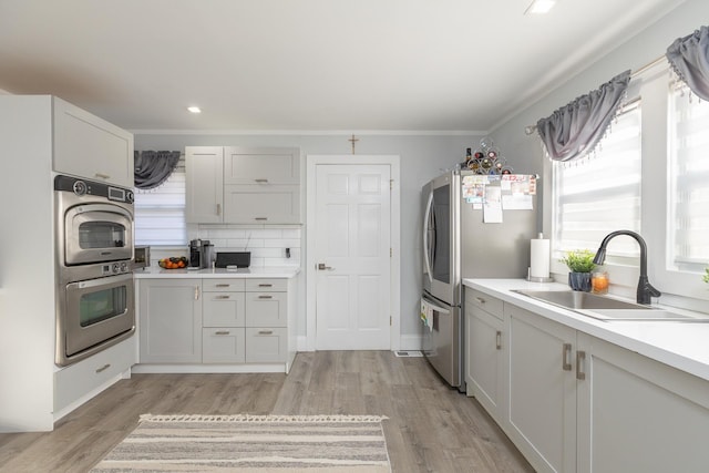 kitchen featuring sink, white cabinetry, tasteful backsplash, light hardwood / wood-style flooring, and appliances with stainless steel finishes