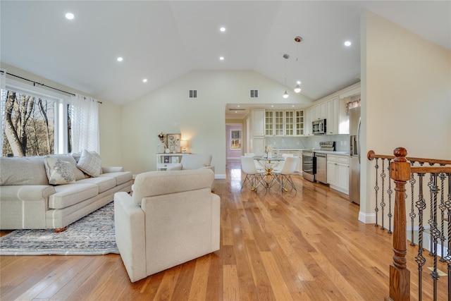 living room featuring high vaulted ceiling, visible vents, light wood-style flooring, and baseboards