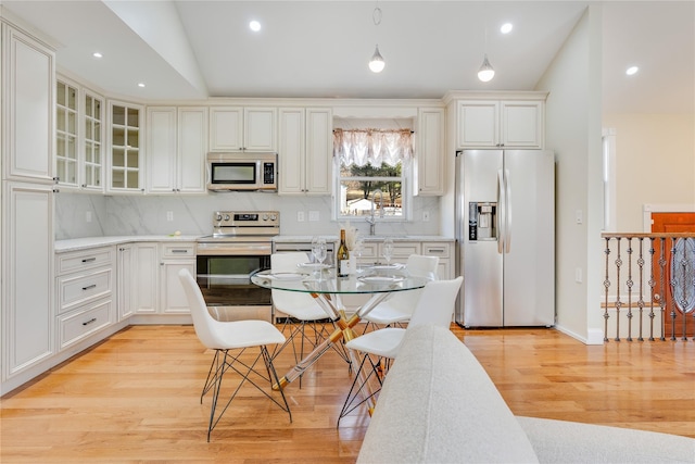 kitchen featuring pendant lighting, light countertops, appliances with stainless steel finishes, glass insert cabinets, and white cabinets