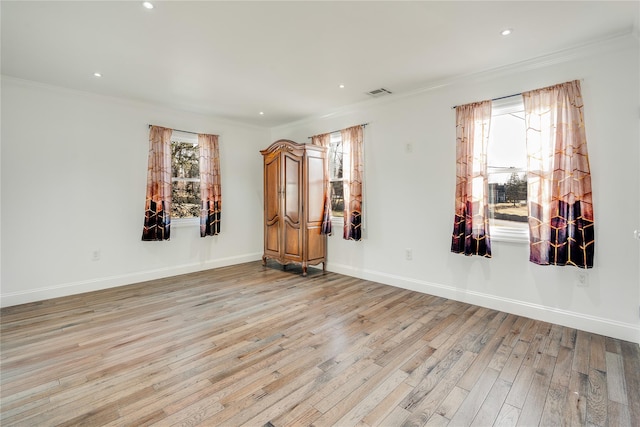 spare room featuring baseboards, light wood finished floors, visible vents, and crown molding