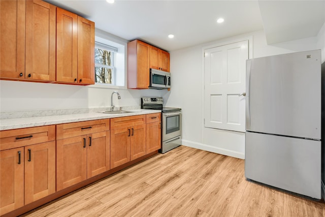 kitchen with light stone counters, stainless steel appliances, sink, and light hardwood / wood-style flooring