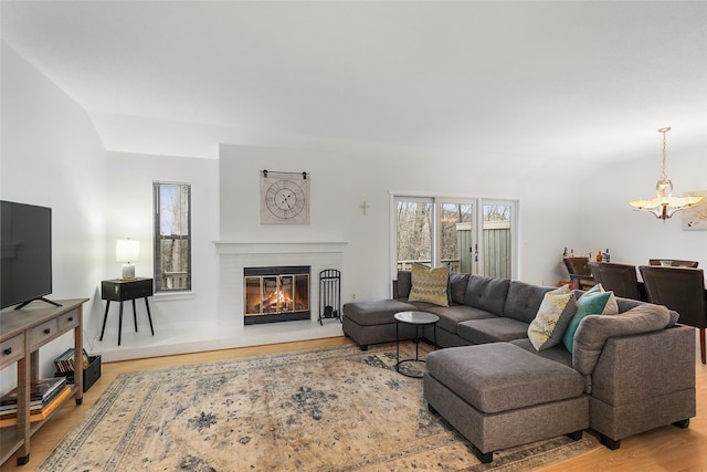 living room with a wealth of natural light, a glass covered fireplace, a notable chandelier, and lofted ceiling