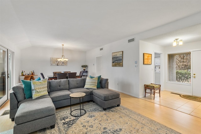 living area with lofted ceiling, wood finished floors, visible vents, and a notable chandelier