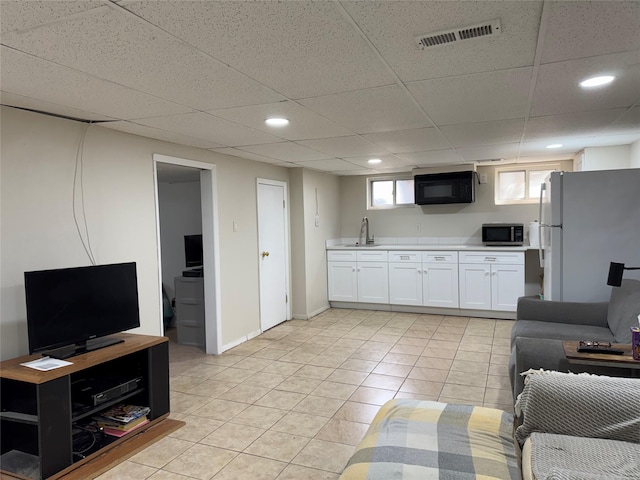 living area with a drop ceiling, visible vents, baseboards, and light tile patterned flooring