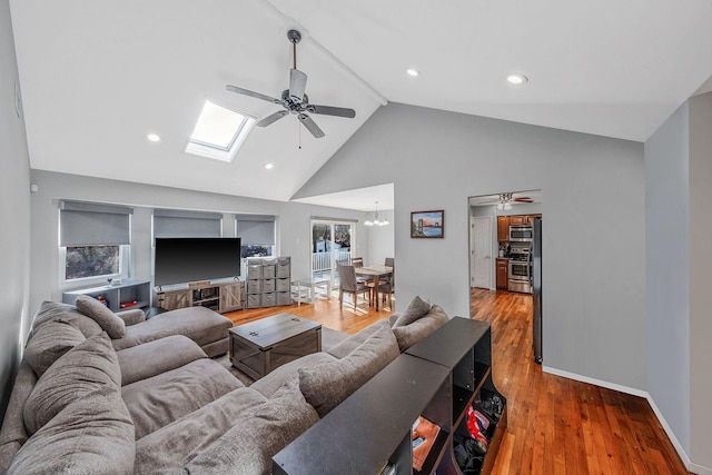 living room featuring high vaulted ceiling, wood-type flooring, a skylight, and ceiling fan with notable chandelier