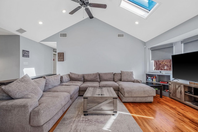 living room featuring wood-type flooring, high vaulted ceiling, ceiling fan, and a skylight