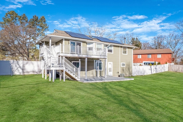 rear view of house featuring central air condition unit, solar panels, a lawn, a deck, and a patio