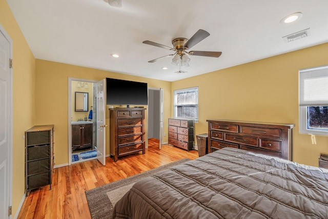 bedroom with multiple windows, ensuite bath, ceiling fan, and light hardwood / wood-style flooring