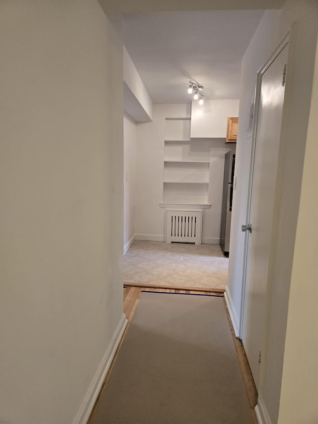 corridor featuring radiator, track lighting, and built in shelves