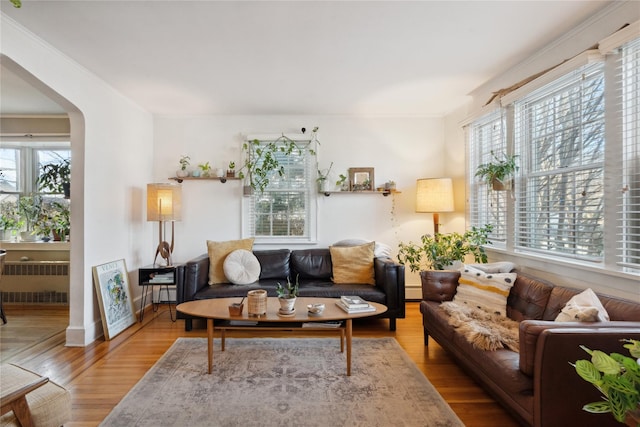 living area featuring arched walkways, crown molding, radiator heating unit, wood finished floors, and baseboards