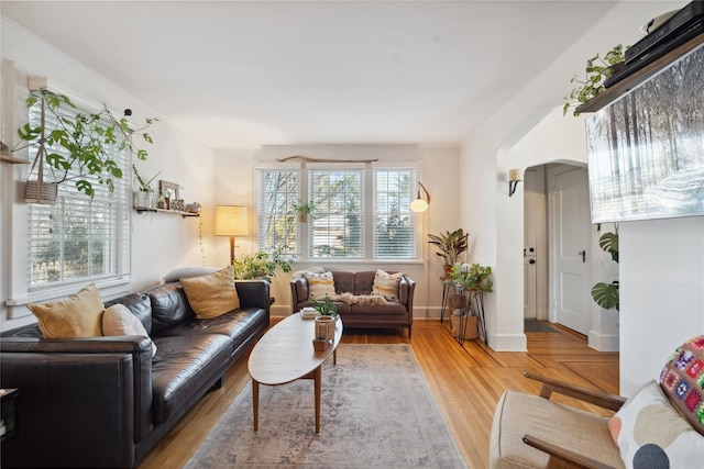 living room featuring arched walkways, light wood finished floors, crown molding, and baseboards