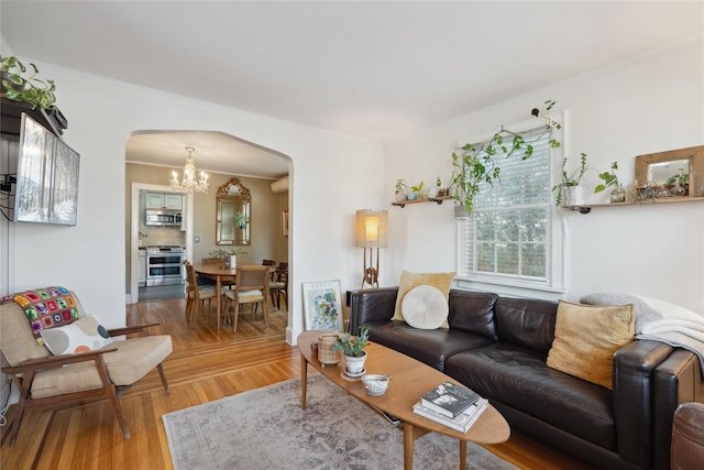 living area with arched walkways, an inviting chandelier, wood finished floors, and crown molding