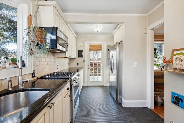 kitchen with decorative backsplash, appliances with stainless steel finishes, dark stone countertops, crown molding, and a sink