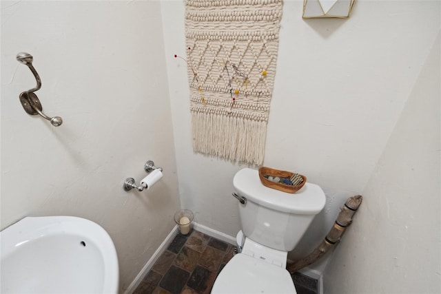 bathroom featuring toilet, stone finish flooring, baseboards, and a sink