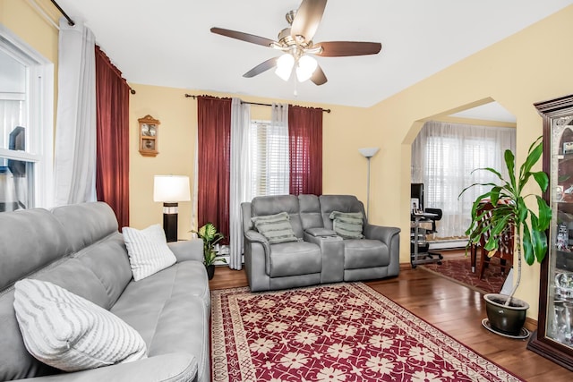 living area with ceiling fan, arched walkways, a baseboard radiator, and wood finished floors