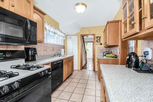 kitchen with light tile patterned floors, glass insert cabinets, light countertops, black appliances, and backsplash