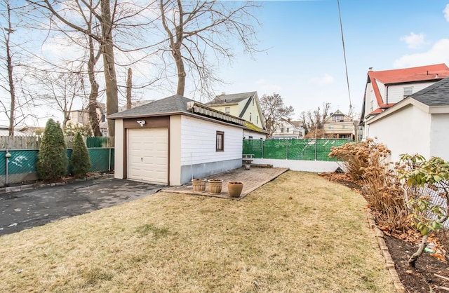 exterior space featuring a shingled roof, an outdoor structure, fence, driveway, and a lawn