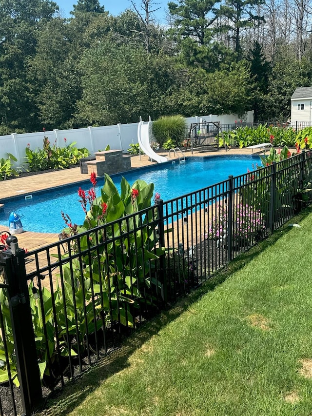 view of pool with a fenced in pool, a lawn, a water slide, a fenced backyard, and a diving board