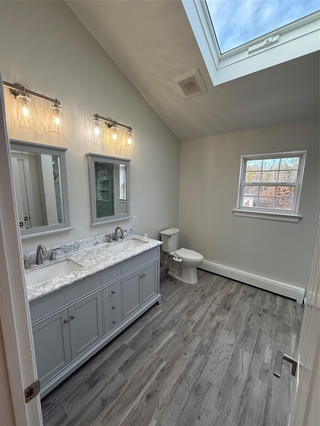 bathroom featuring wood finished floors, lofted ceiling with skylight, a sink, and visible vents