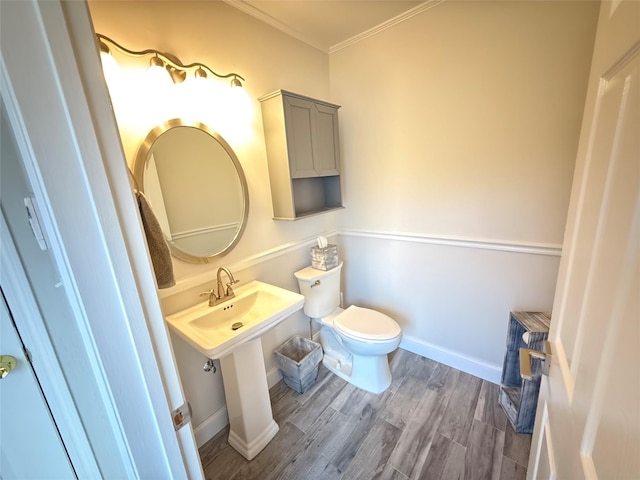 half bathroom with baseboards, crown molding, toilet, and wood finished floors