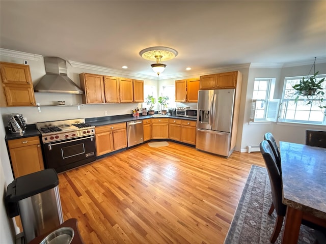 kitchen featuring dark countertops, light wood-style flooring, ornamental molding, stainless steel appliances, and wall chimney range hood