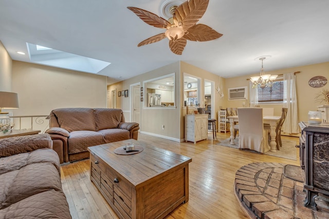 living room with a wall mounted AC, a skylight, ceiling fan with notable chandelier, and light wood-type flooring