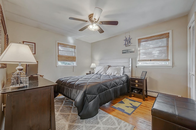 bedroom with multiple windows, ceiling fan, a baseboard heating unit, and light wood-type flooring