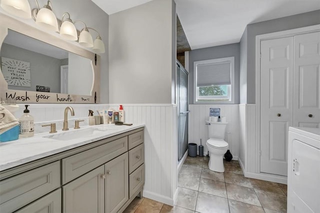 bathroom with a shower with shower door, washer / dryer, tile patterned flooring, vanity, and toilet