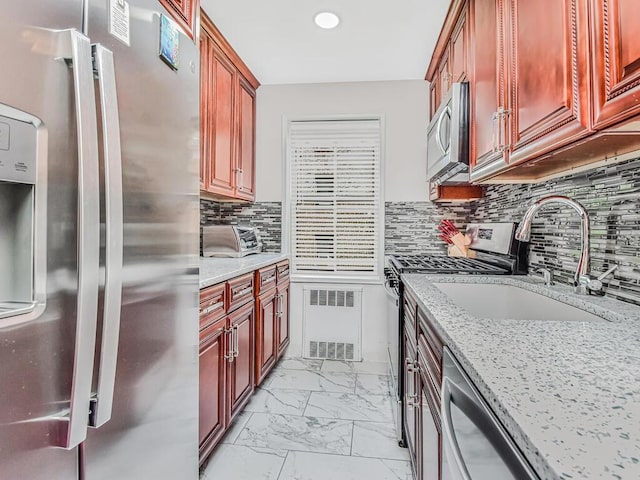 kitchen featuring sink, light stone counters, tasteful backsplash, radiator, and stainless steel appliances