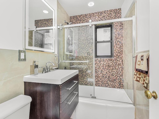 full bathroom featuring vanity, toilet, combined bath / shower with glass door, and tile walls