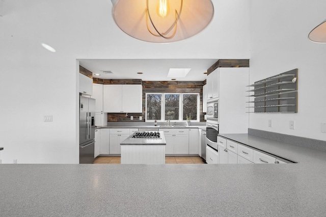 kitchen with a skylight, white cabinetry, backsplash, kitchen peninsula, and stainless steel appliances