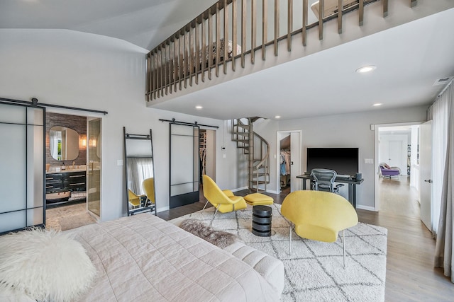 bedroom featuring a spacious closet, light wood-type flooring, a closet, a barn door, and a high ceiling