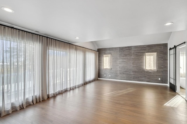 empty room featuring wood-type flooring, a barn door, and vaulted ceiling