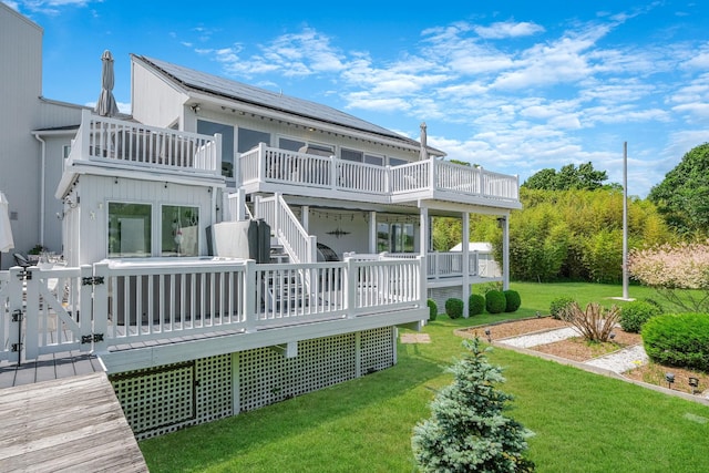 back of house with a balcony, a yard, a deck, and solar panels