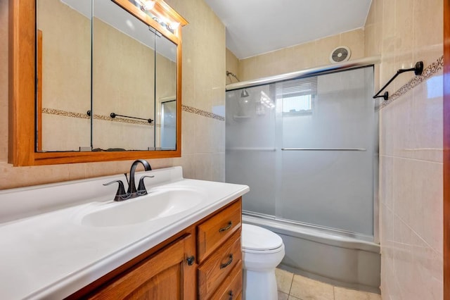 full bathroom featuring toilet, combined bath / shower with glass door, tile walls, vanity, and tile patterned flooring