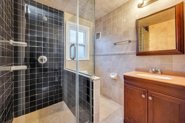 bathroom with vanity, a shower with door, and tile walls