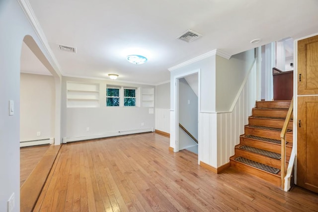 basement with ornamental molding, a baseboard heating unit, built in features, and light wood-type flooring