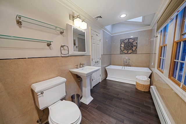 bathroom featuring a tub to relax in, toilet, crown molding, tile walls, and baseboard heating