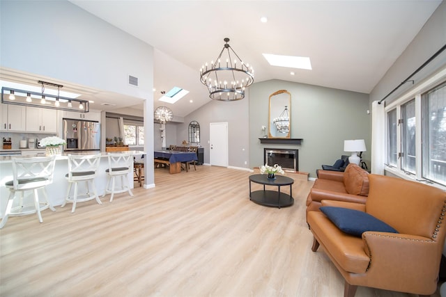 living room with high vaulted ceiling, a chandelier, light hardwood / wood-style floors, and a skylight