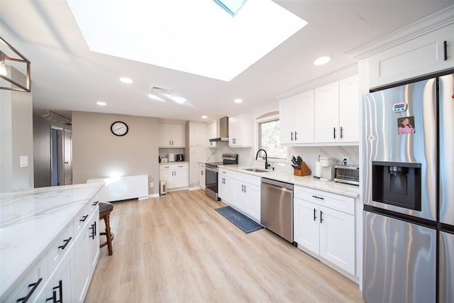 kitchen with wall chimney exhaust hood, sink, white cabinetry, light stone counters, and appliances with stainless steel finishes