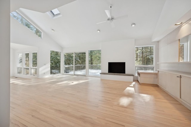 unfurnished living room with light hardwood / wood-style flooring, a skylight, high vaulted ceiling, ceiling fan, and a fireplace