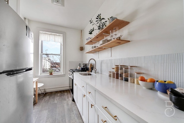 kitchen with appliances with stainless steel finishes, tasteful backsplash, white cabinetry, sink, and light hardwood / wood-style floors