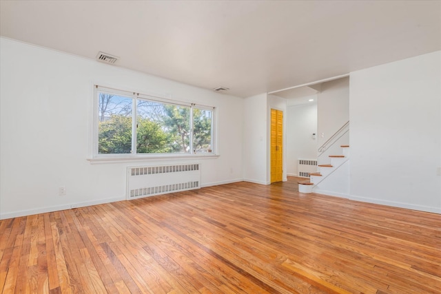 unfurnished room featuring light wood-style flooring, radiator heating unit, visible vents, and stairway