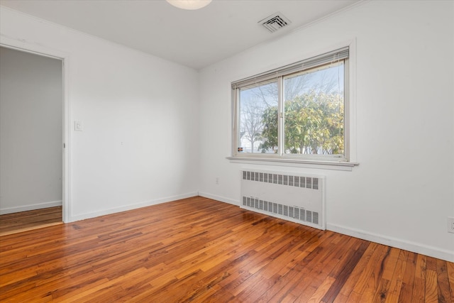 empty room featuring baseboards, visible vents, radiator, ornamental molding, and wood finished floors