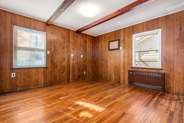 unfurnished room featuring wooden walls, radiator, beamed ceiling, and light wood-style flooring